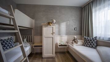 A bedroom with bunk beds, a wardrobe, a bedside table with a teddy bear, and a window with curtains.
