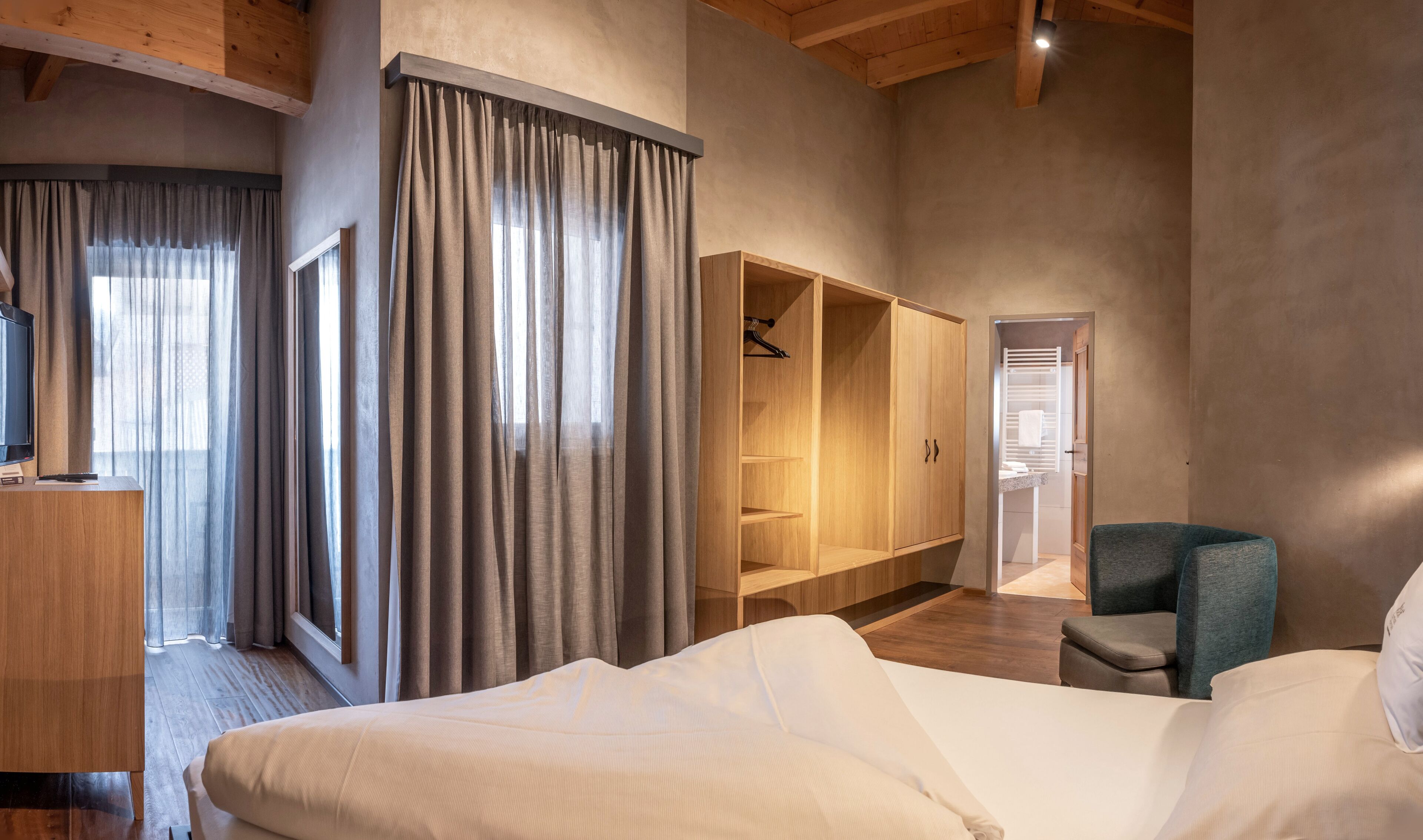 A hotel room with a bed, a desk with a TV, a wardrobe, and a seating area.