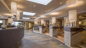 A spacious lobby with a curved reception desk, a staircase, and modern pendant lighting. - Familienparadies Sporthotel Achensee - All Inclusive (Achenkirch)