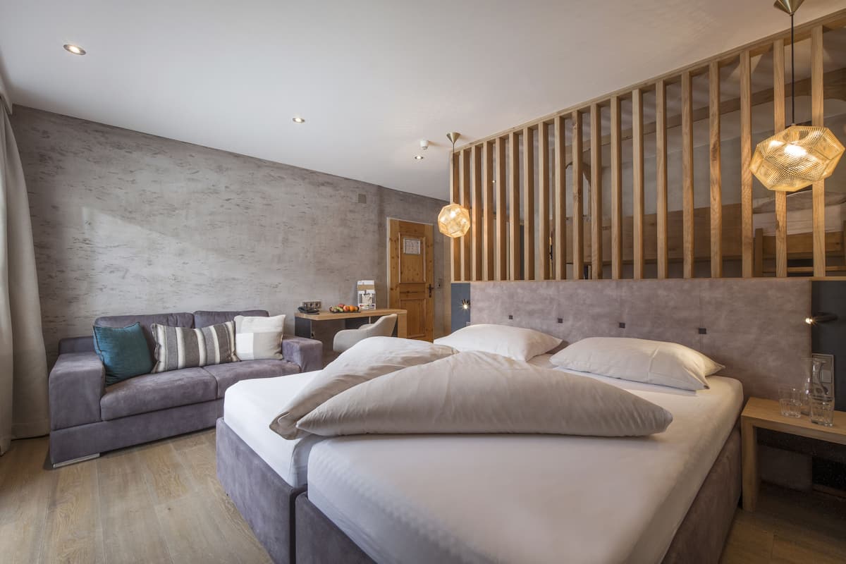 A modern hotel room with a large bed, a sofa, a wooden partition, and a dining area.