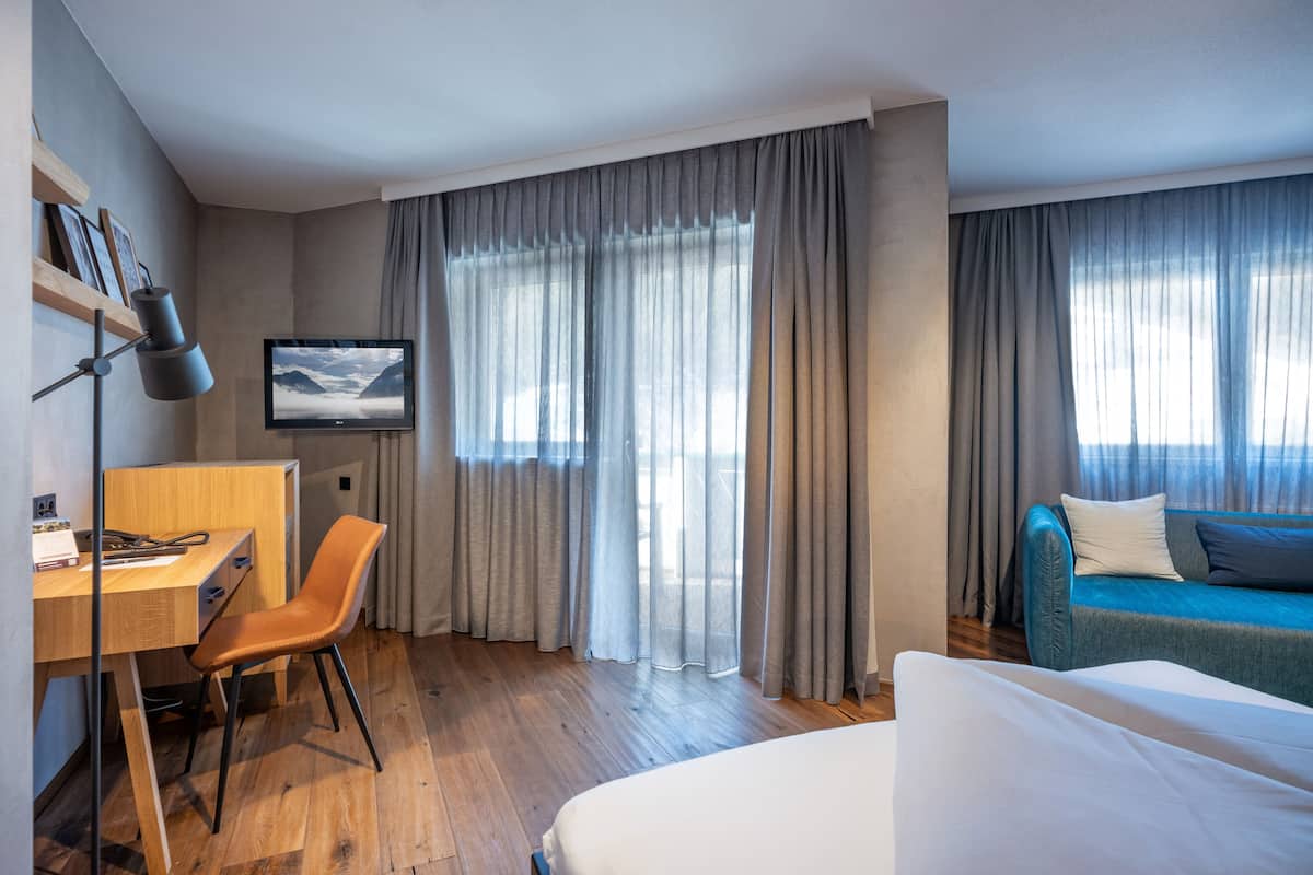 A hotel room with a wooden desk, a chair, a bed, a TV, and a sofa.