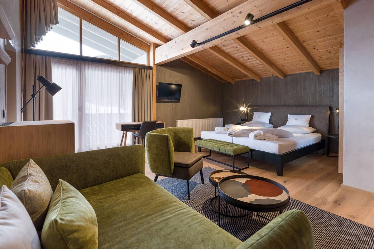 A modern bedroom with a wooden ceiling, a bed with white linens, a desk, and a green sofa.