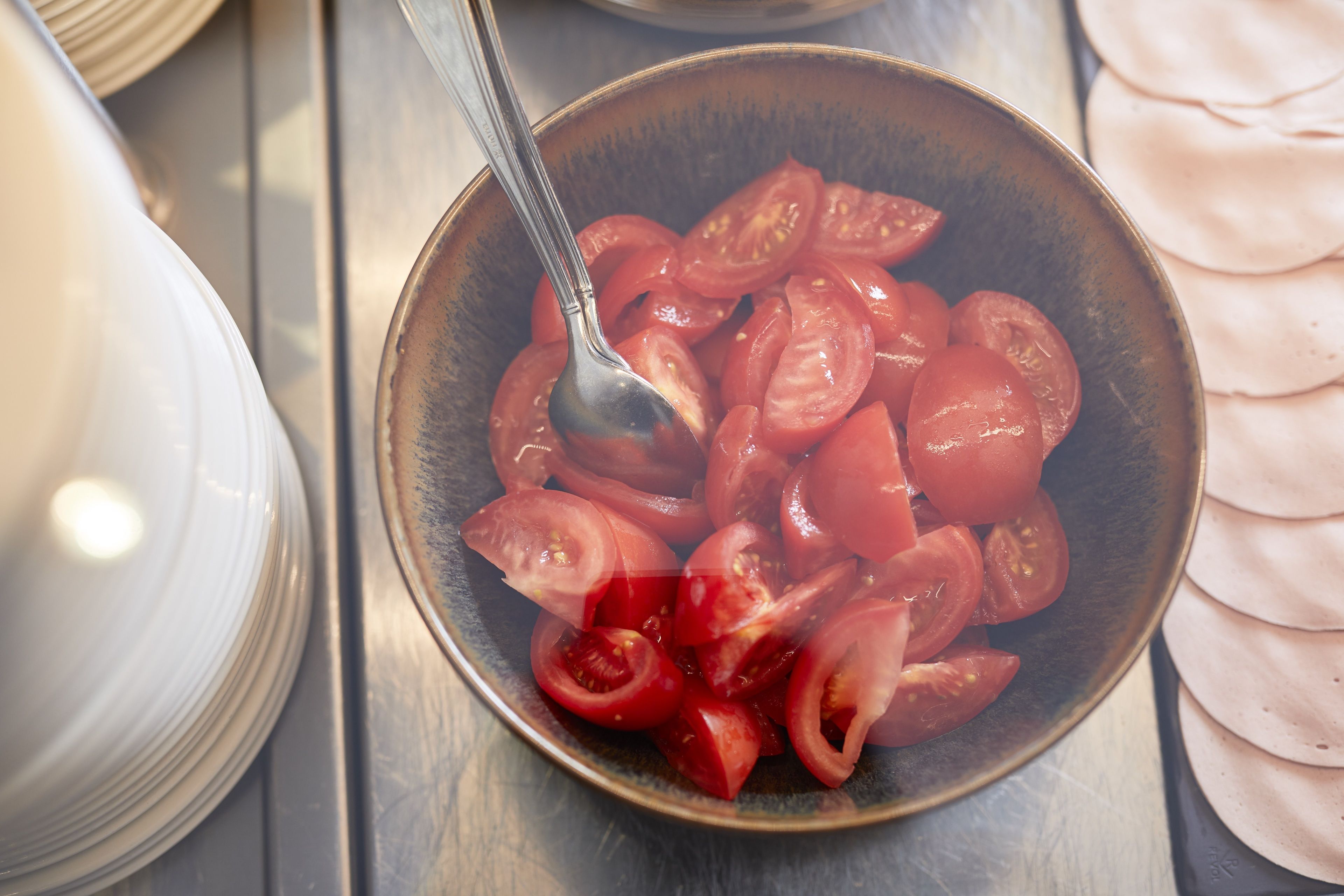 A bowl of sliced tomatoes with a spoon.