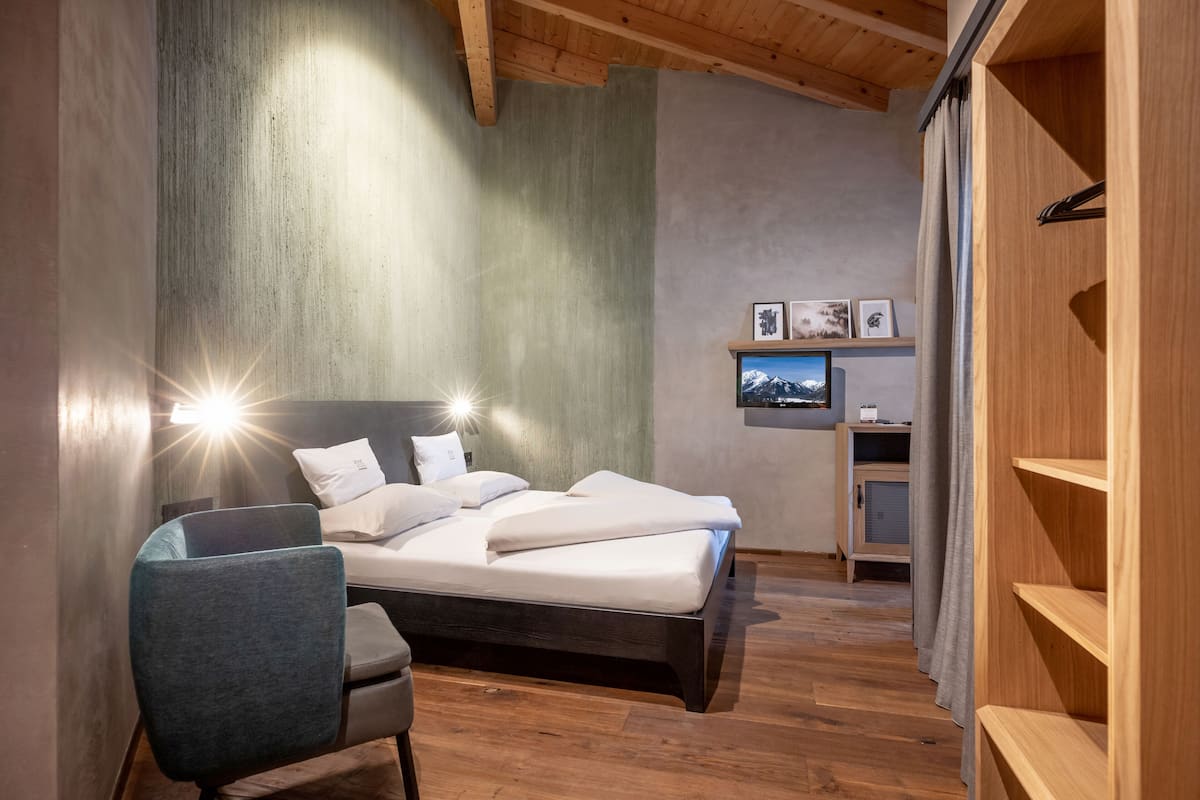 A modern bedroom with a bed, a chair, a desk, and a TV on a shelf.