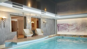 An indoor swimming pool with a clear view of the water, a set of wicker chairs, and a large abstract painting on the wall. - Familienparadies Sporthotel Achensee - All Inclusive (Achenkirch)
