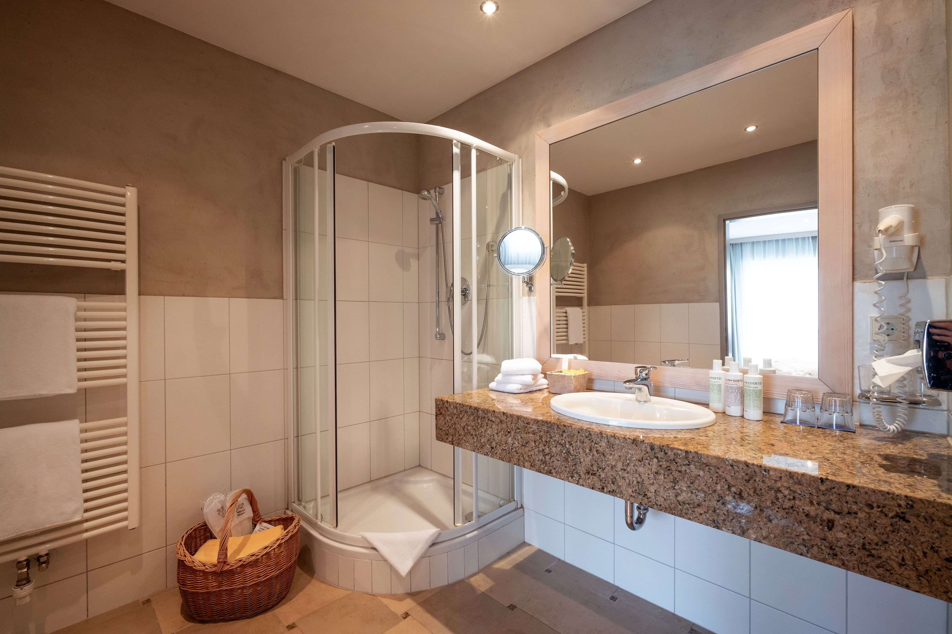 A modern bathroom with a glass-enclosed shower, a granite countertop, a large mirror, and a towel rack.