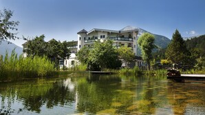 A hotel with a large building, a lake, and mountains in the background. - Familienparadies Sporthotel Achensee - All Inclusive (Achenkirch)