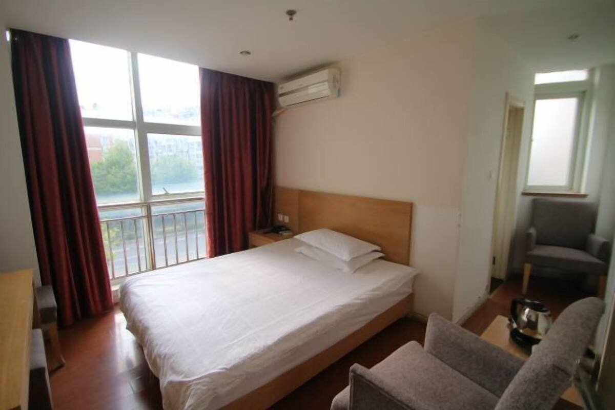 Habitación de hotel con una cama individual, una silla, una mesita y una ventana con cortinas.
