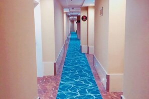 Un couloir d’hôtel avec un tapis à motifs, des murs de couleur beige et un mur d’accent bleu.