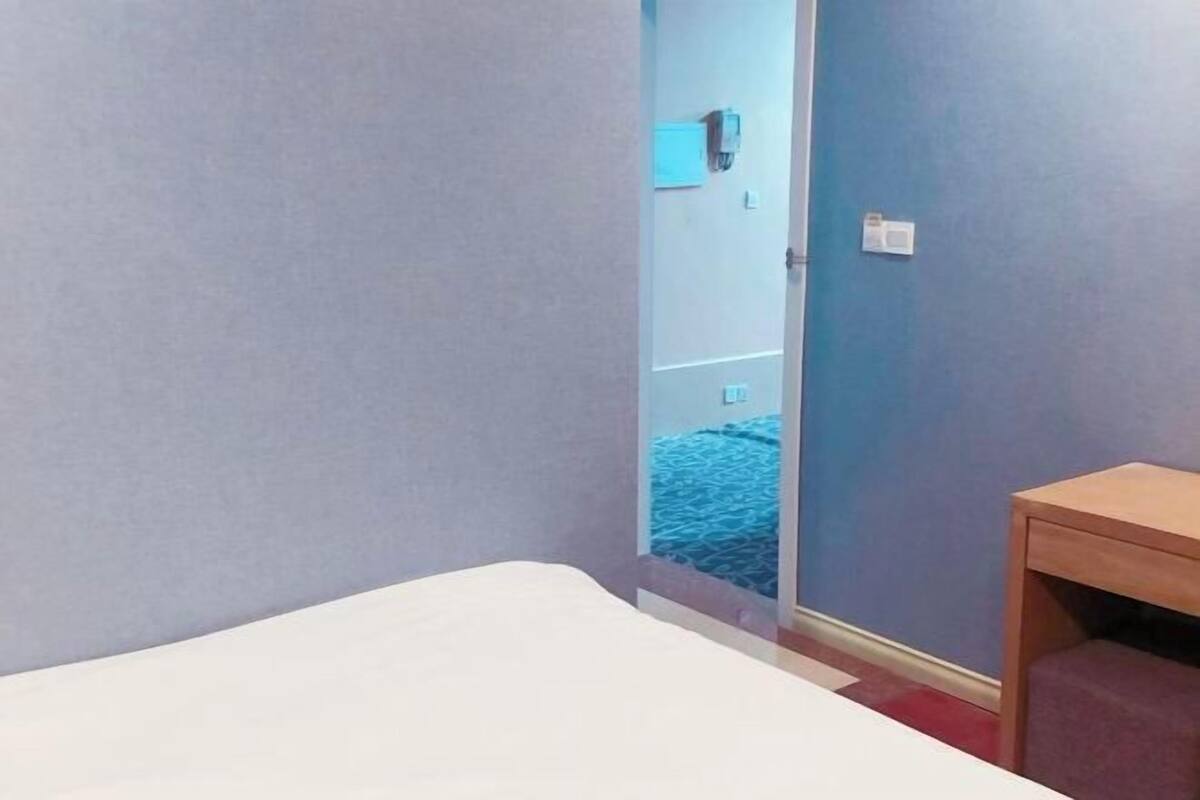 Habitación de hotel con cama, una pequeña mesa de madera y vista a una pared azul y una puerta que da a otra habitación.