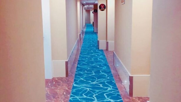 Un pasillo de hotel con alfombra azul estampada, paredes color beige y suelo de baldosas rojas.