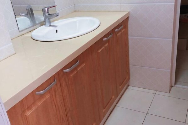Un baño con lavamanos blanco, armarios de madera y un espejo.