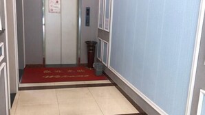Un pasillo con alfombra roja, un bote de basura y un cartel en la puerta.