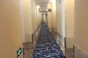 Un couloir d’hôtel avec un tapis à motifs, des portes de chaque côté et une horloge au mur.