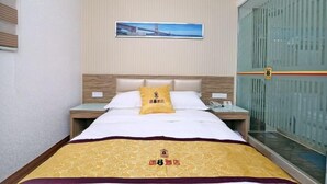 Una habitación de hotel con cama, mesita de noche, un cuadro colgado en la pared y una puerta corrediza.