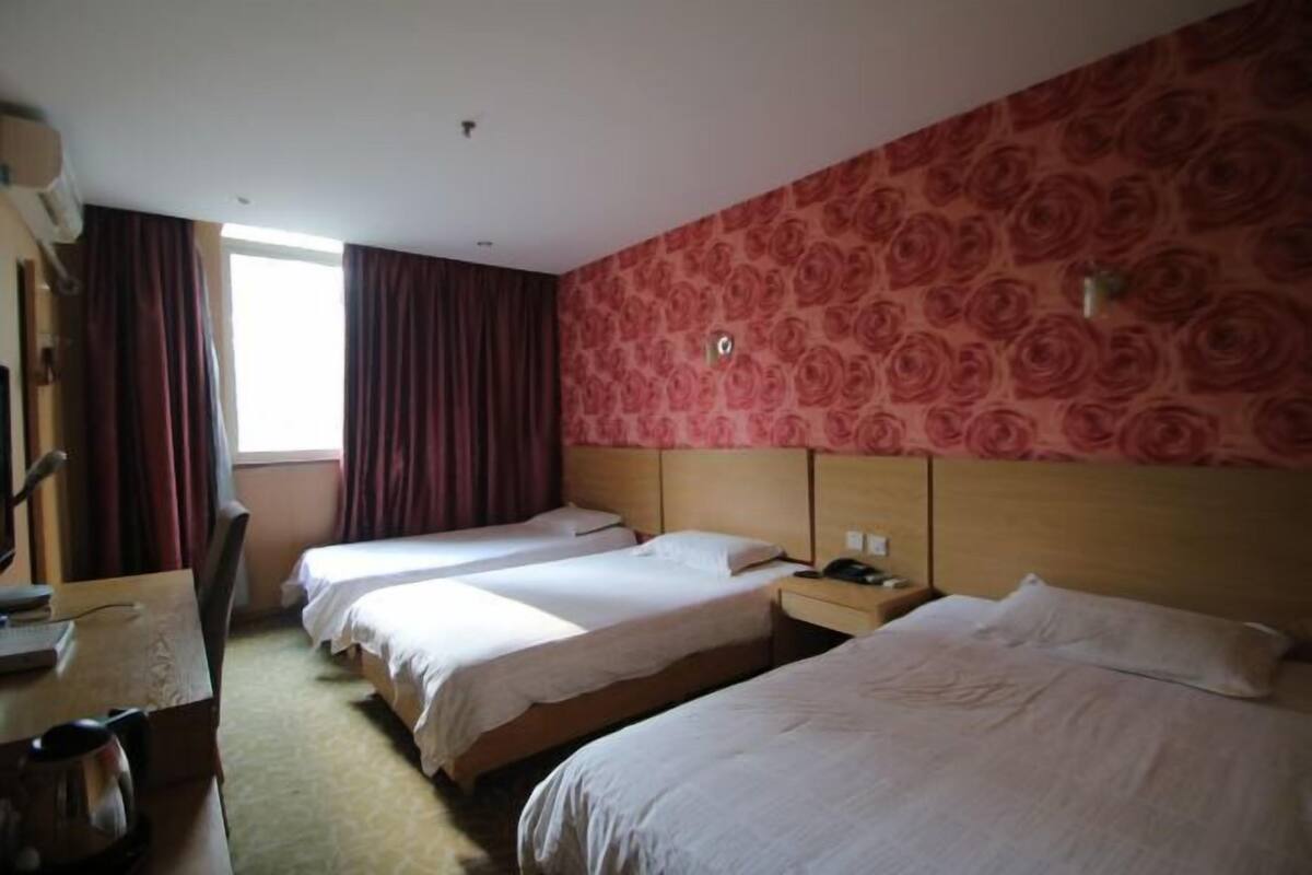 Habitación de hotel con tres camas, un escritorio, una silla, una ventana con cortinas y una pared con estampado floral.