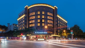 A multi-story hotel with a curved facade, illuminated windows, and a sign indicating it is a hotel. - Minshan Lhasa Grand Hotel (Chengdu)