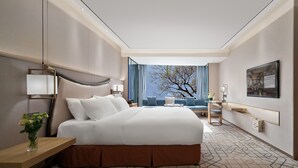 A modern hotel room with a large bed, a desk, a chair, a sofa, and a view of the outdoors. - Minshan Lhasa Grand Hotel (Chengdu)