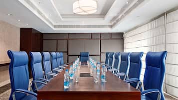 Une salle de conférence avec une longue table en bois, des chaises bleues et des bouteilles d’eau.