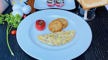 Une assiette contenant une omelette, deux aliments frits, une tomate et deux pots de ketchup, le tout présenté sur une assiette blanche.