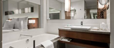 Un baño moderno con un espejo grande, una bañera, un lavabo y un mueble de tocador con un perchero.