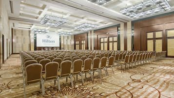 A large conference room with rows of chairs, a Hilton logo, and a patterned carpet.