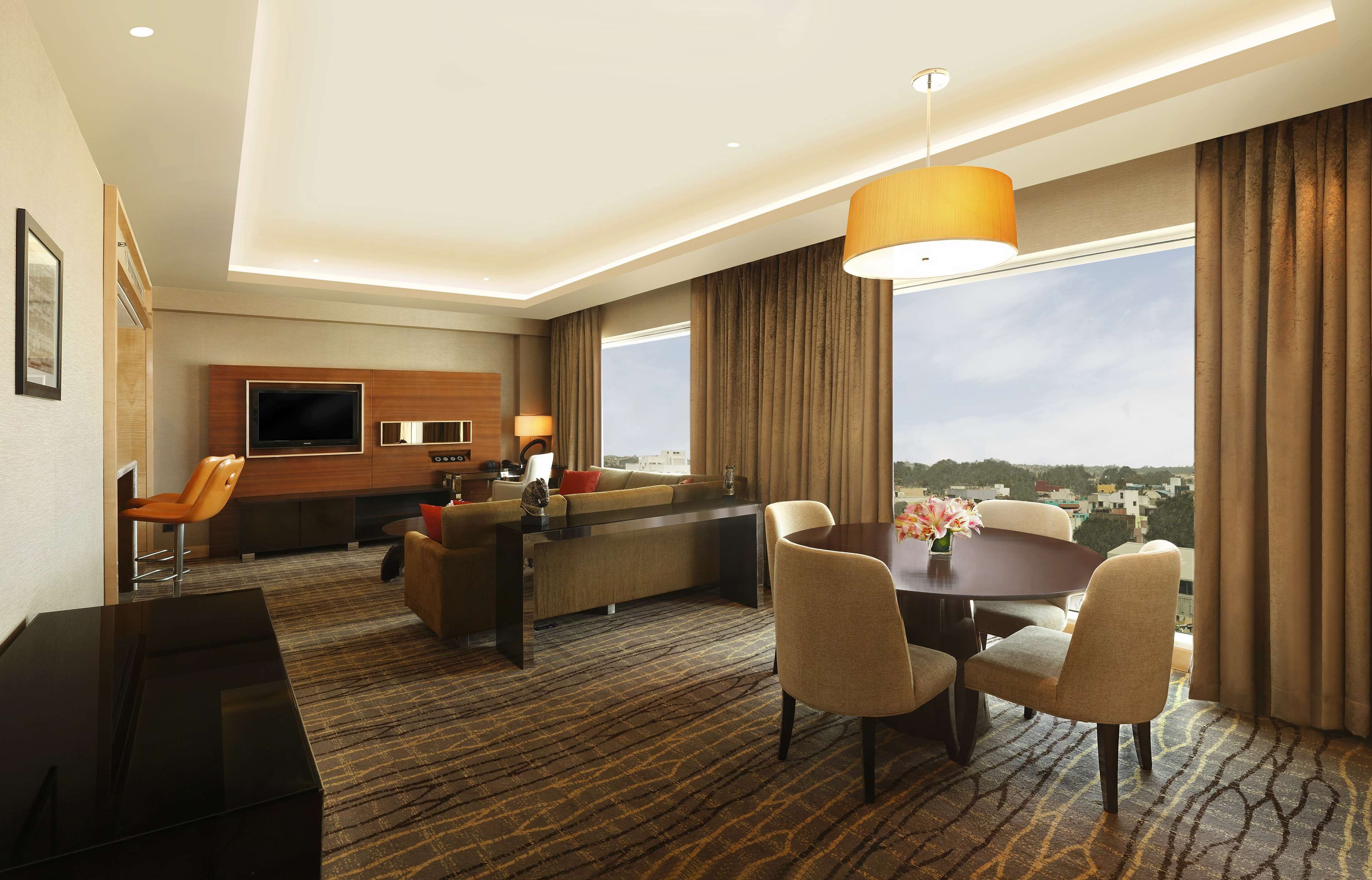 Una habitación de hotel moderna con sofá, mesa de comedor, sillas, televisión y un amplio ventanal con vistas.