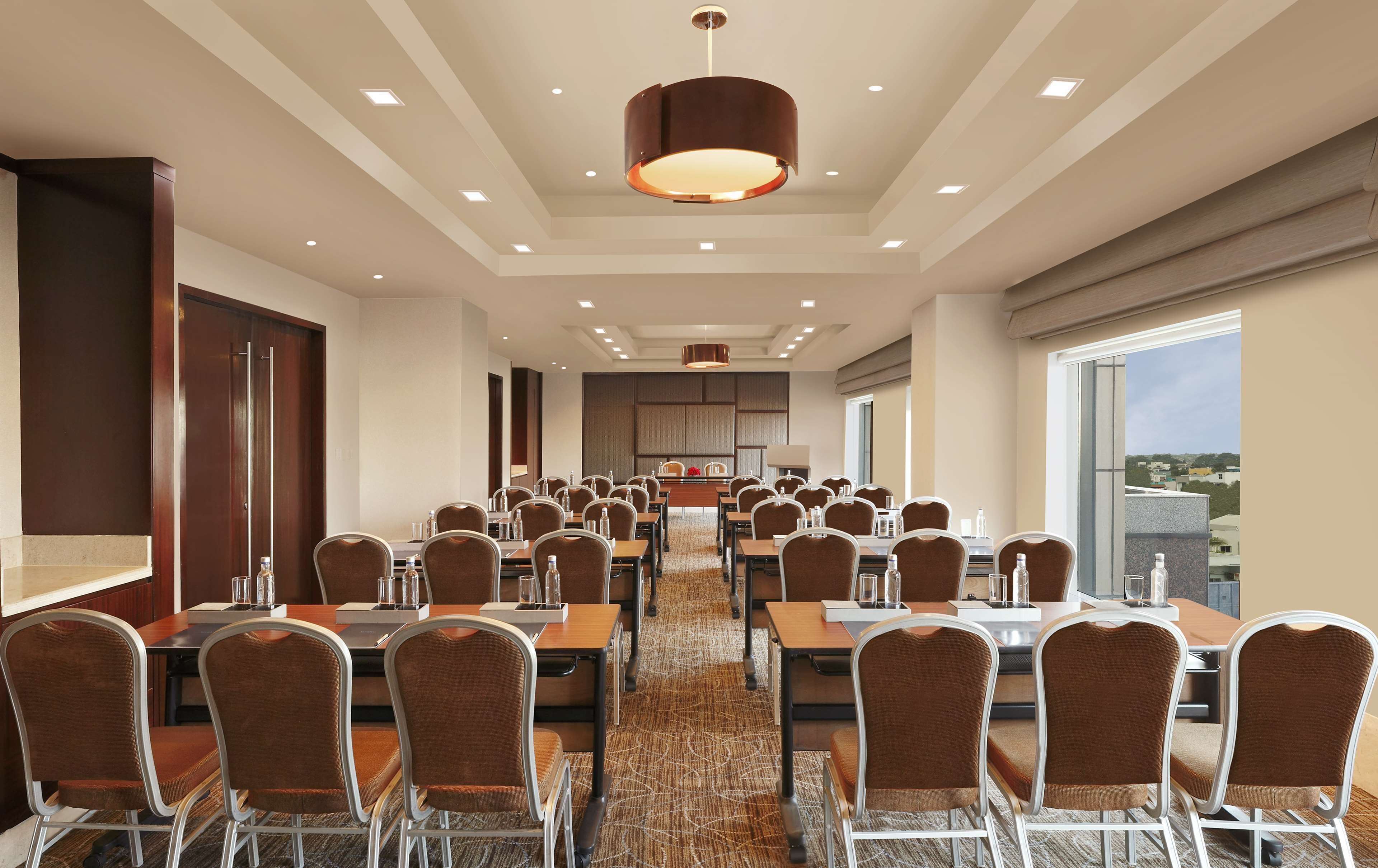 Una sala conferenze con diversi tavoli e sedie, un grande lampadario e vista sulla città attraverso ampie finestre.