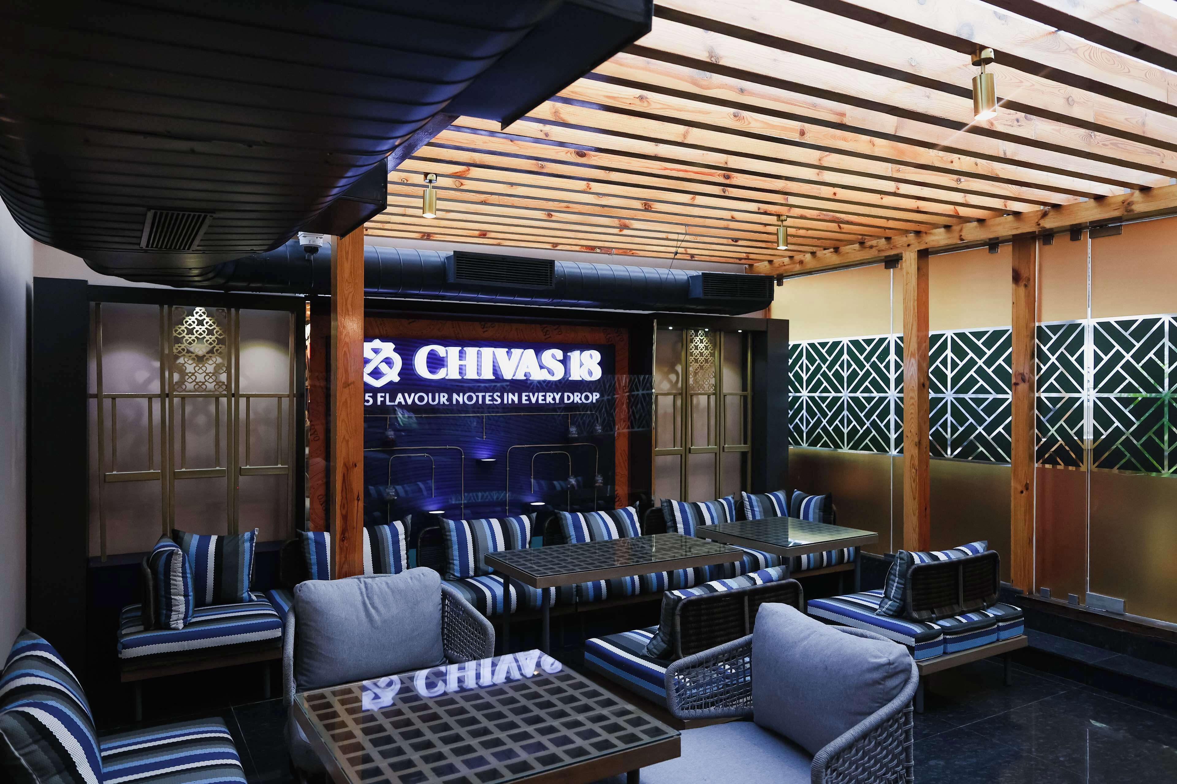 Restaurant amb terrassa, un cartell que diu "CHIVAS 18" i una paret de rajoles amb un disseny geomètric.