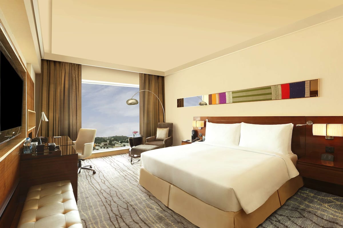 Una habitación de hotel con una cama grande, un escritorio con una silla, un televisor y una ventana con cortinas.
