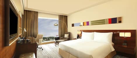 A hotel room with a large bed, a desk with a chair, a TV, and a window with curtains.