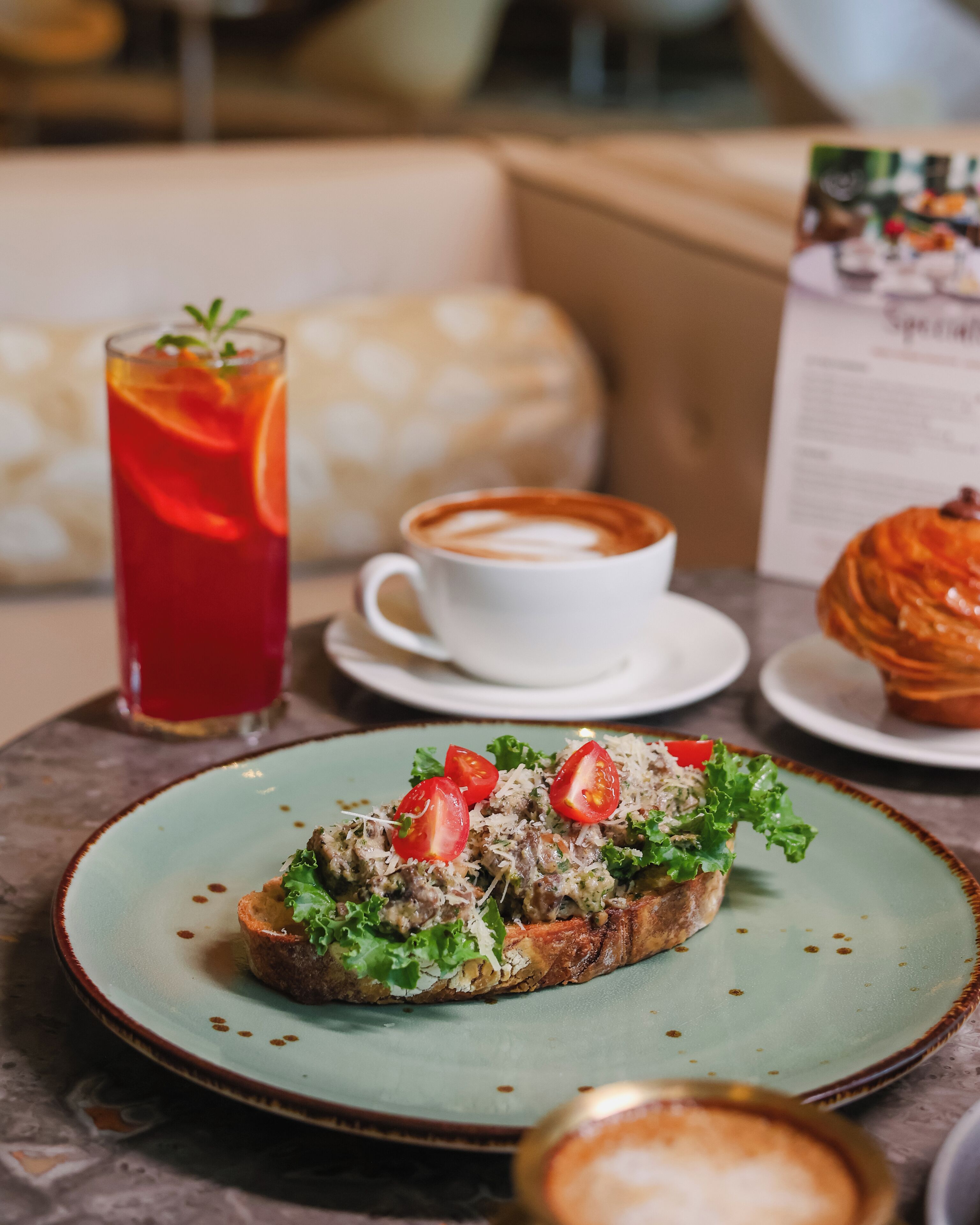 Une table avec une assiette de bruschettas garnies de tomates et de verdure, une tasse de café et un grand verre de thé glacé.