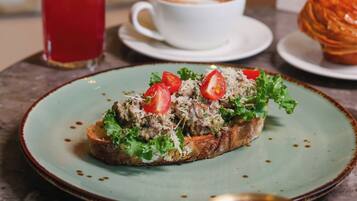 A table with a plate of bruschetta topped with tomatoes and greens, a cup of coffee, and a tall glass of iced tea.