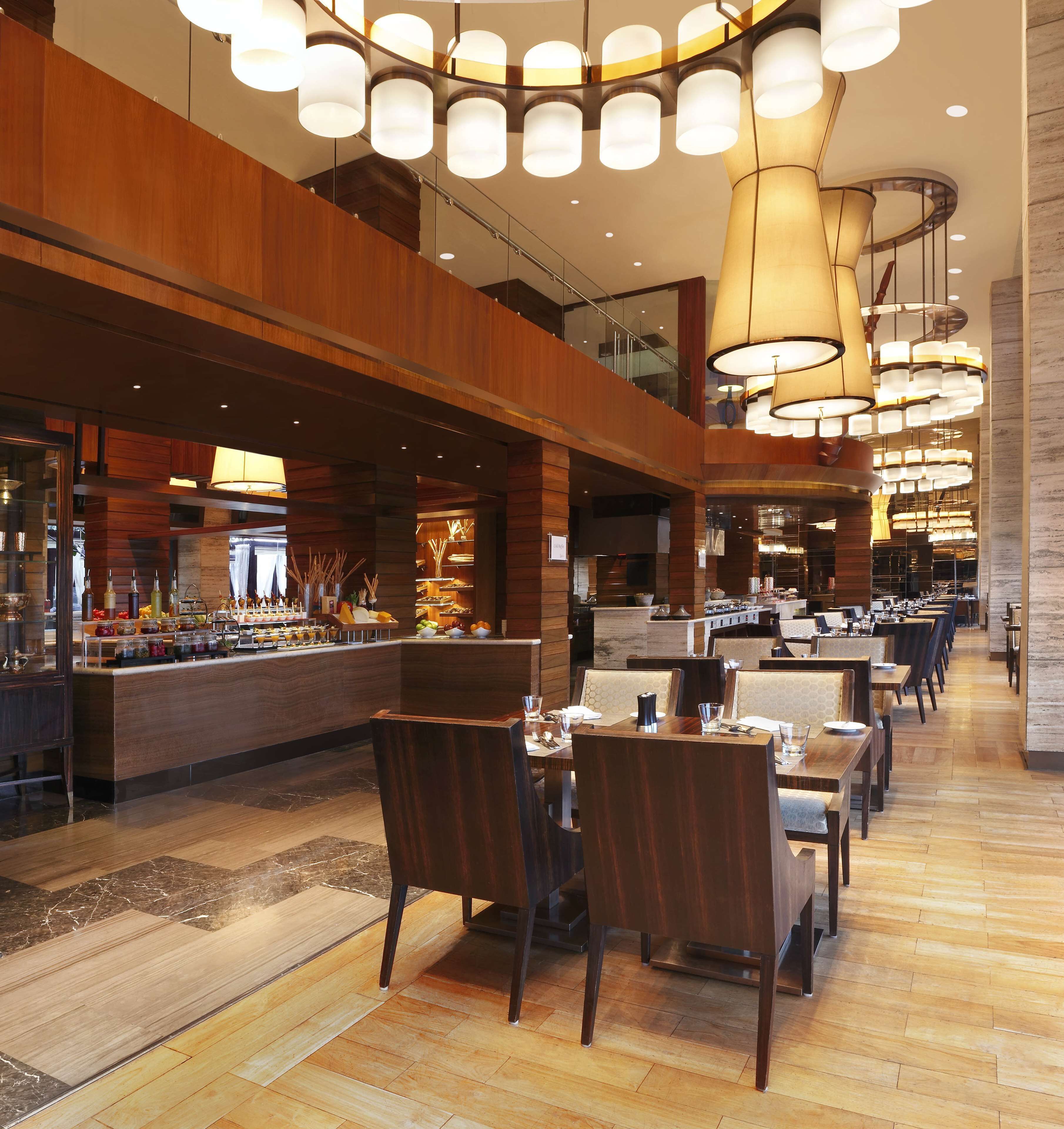 Un hall d’hôtel spacieux doté d’un bar central, de plusieurs espaces salon et d’un plafond haut orné de luminaires modernes.