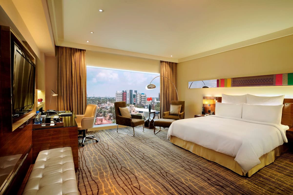 Habitación de hotel con una cama grande, un escritorio con una silla, un sofá y vistas a la ciudad.