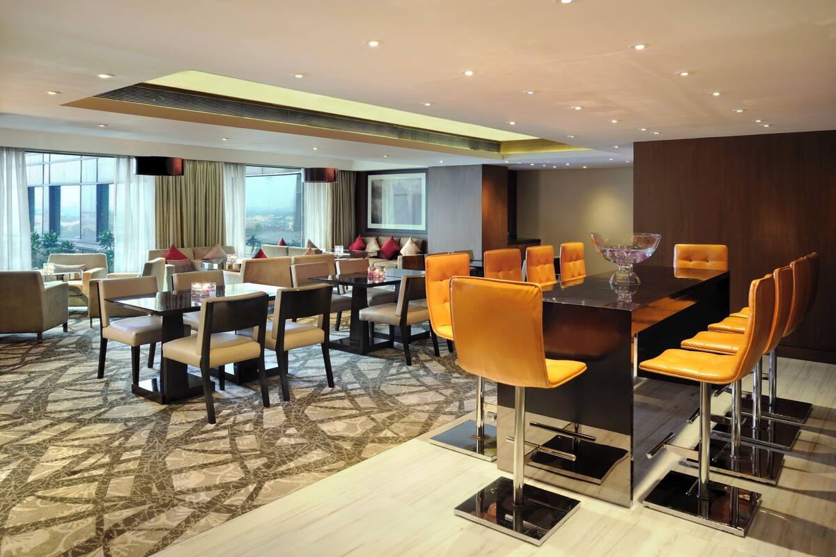 Un comedor de hotel moderno con una mezcla de mesas altas y bajas, asientos cómodos y un amplio ventanal con vistas a la ciudad.