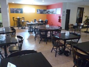 A dining area with multiple tables and chairs, a red accent wall, and a fire extinguisher mounted on the wall.