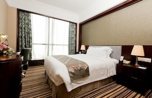 A hotel room with a large bed, a desk with a lamp, a chair, and a nightstand with a phone and lamp.