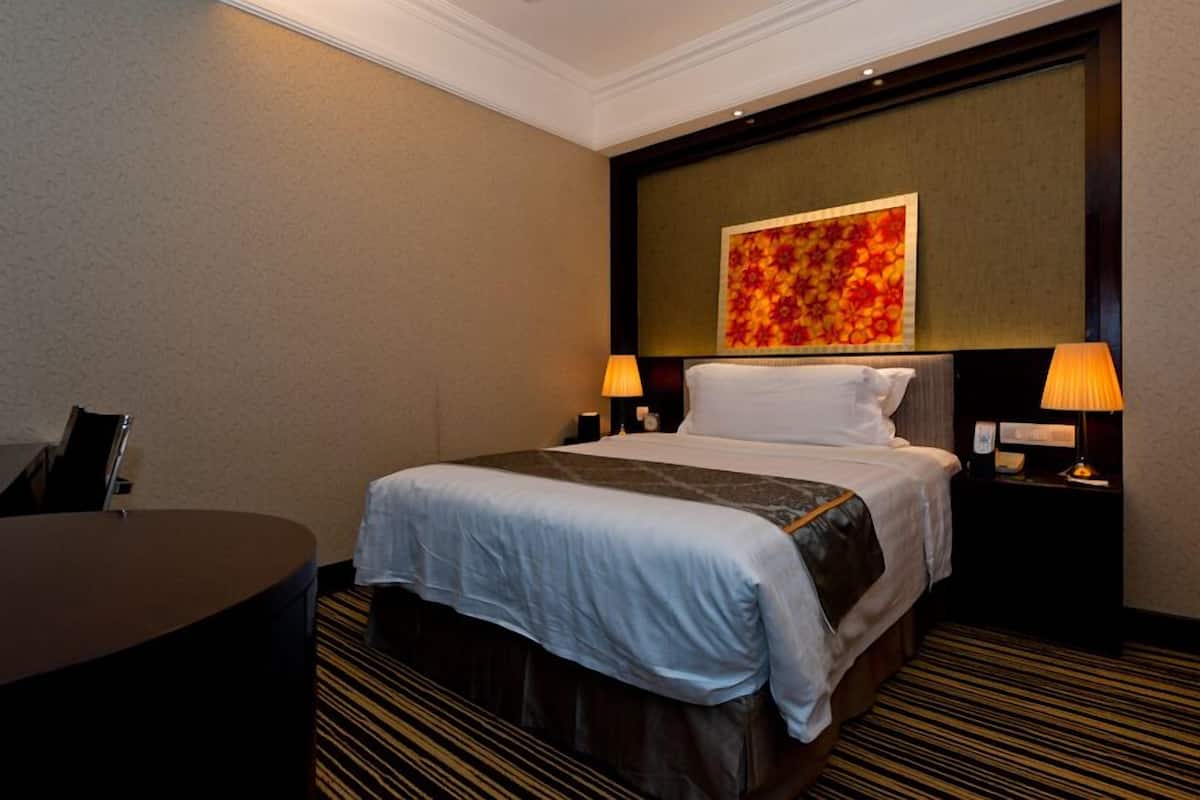 Quarto de hotel com cama grande, duas luminárias de cabeceira, uma escrivaninha e um objeto decorativo na parede.