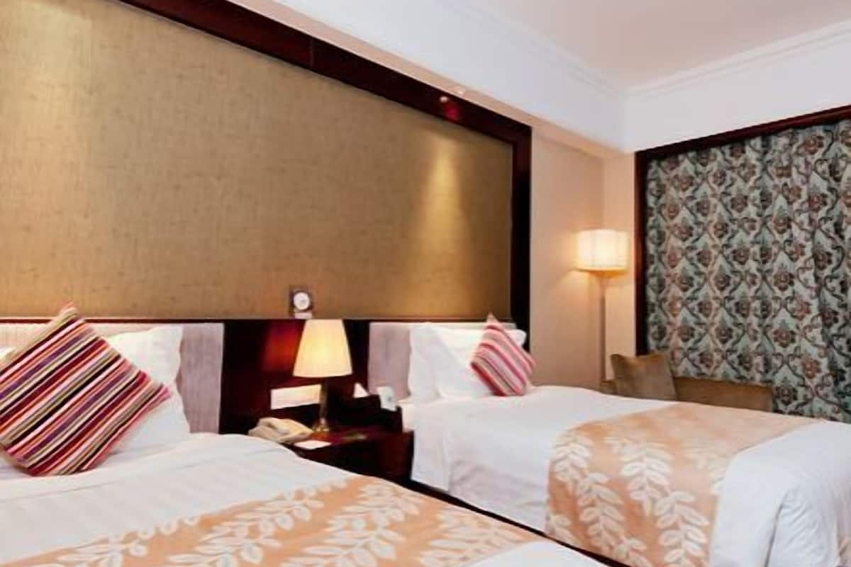 Quarto de hotel com duas camas, uma mesa de cabeceira com abajur e papel de parede estampado.
