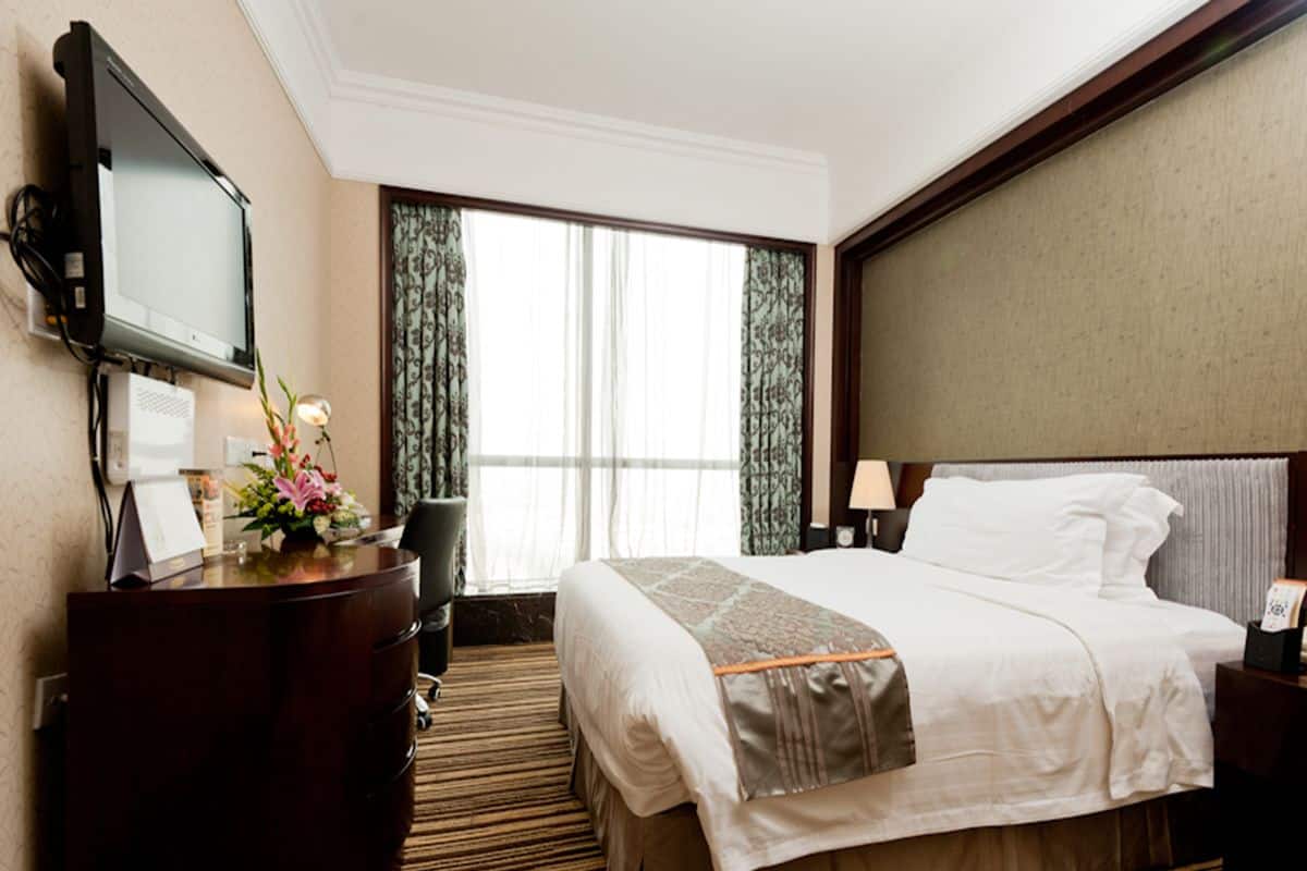 Quarto de hotel com uma cama grande, uma escrivaninha com televisão de tela plana, cômoda e janela com cortinas.