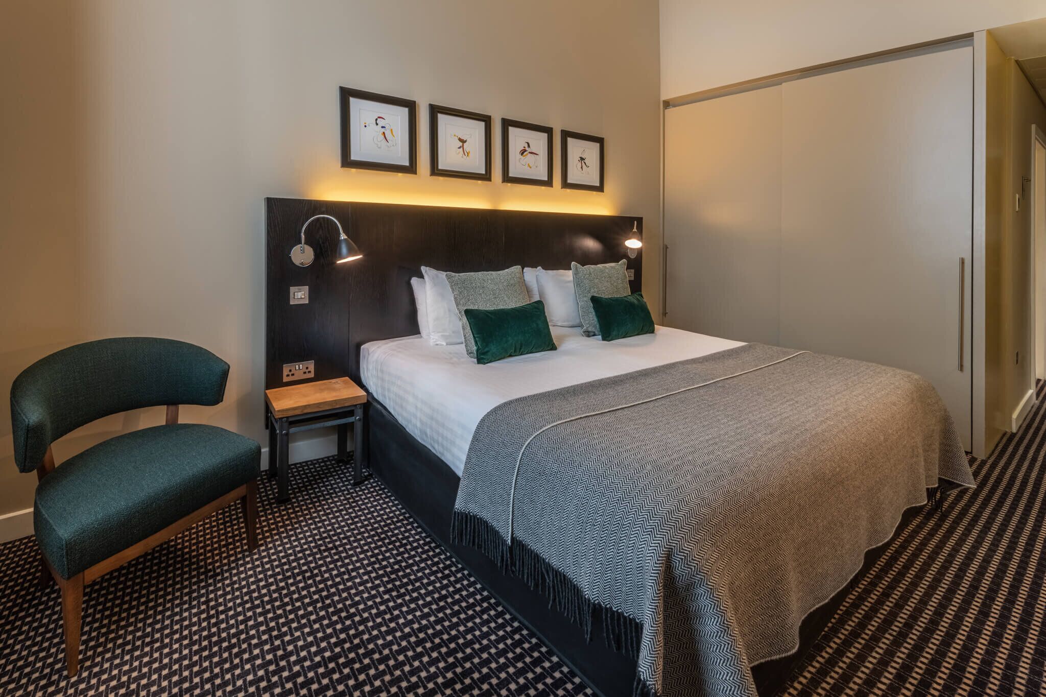 A hotel room with a bed, a chair, a nightstand, a lamp, and a wardrobe.