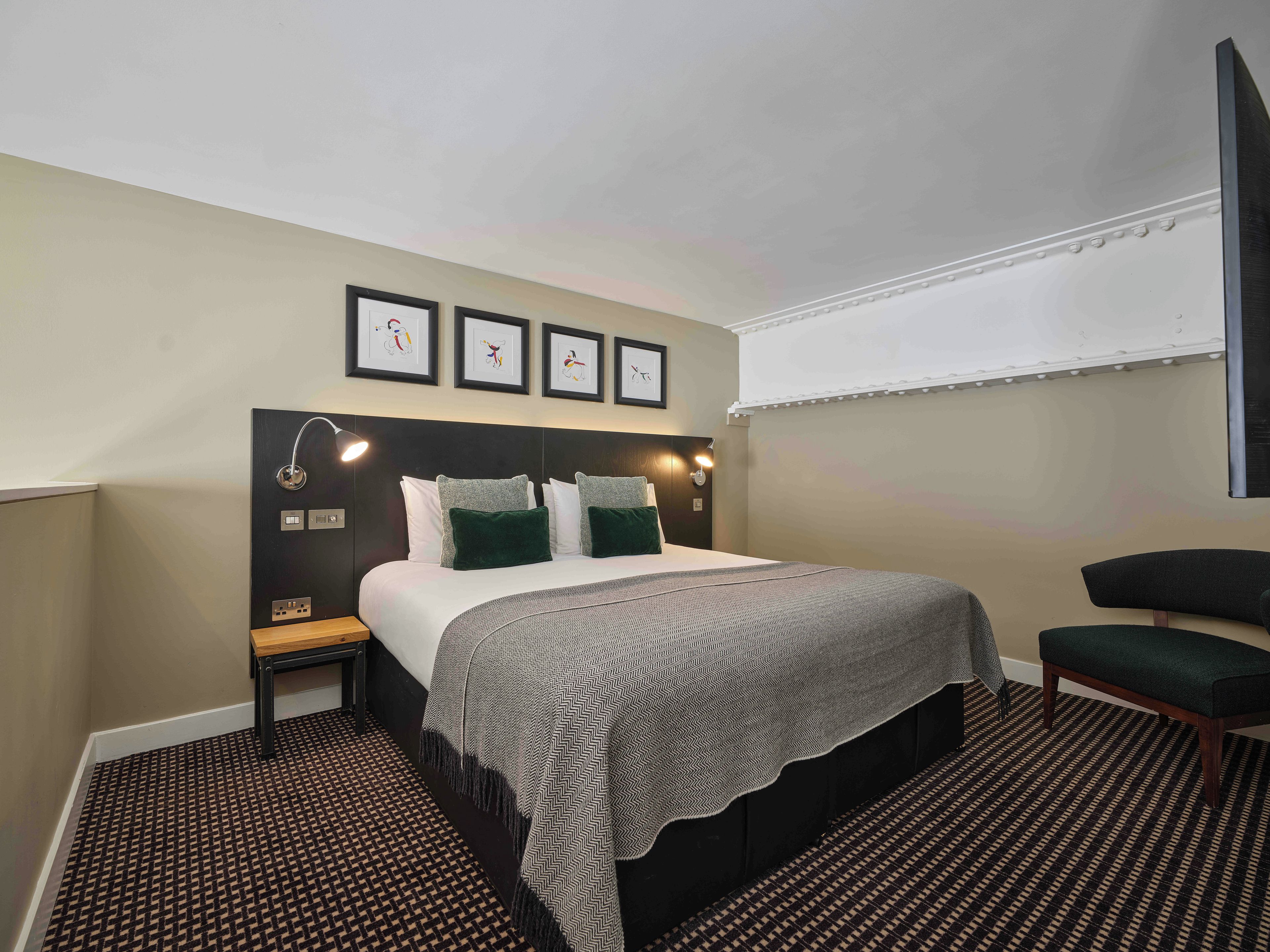 A hotel room with a bed, bedside tables, a chair, and artwork on the wall.