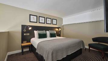 A hotel room with a bed, bedside tables, a chair, and artwork on the wall.