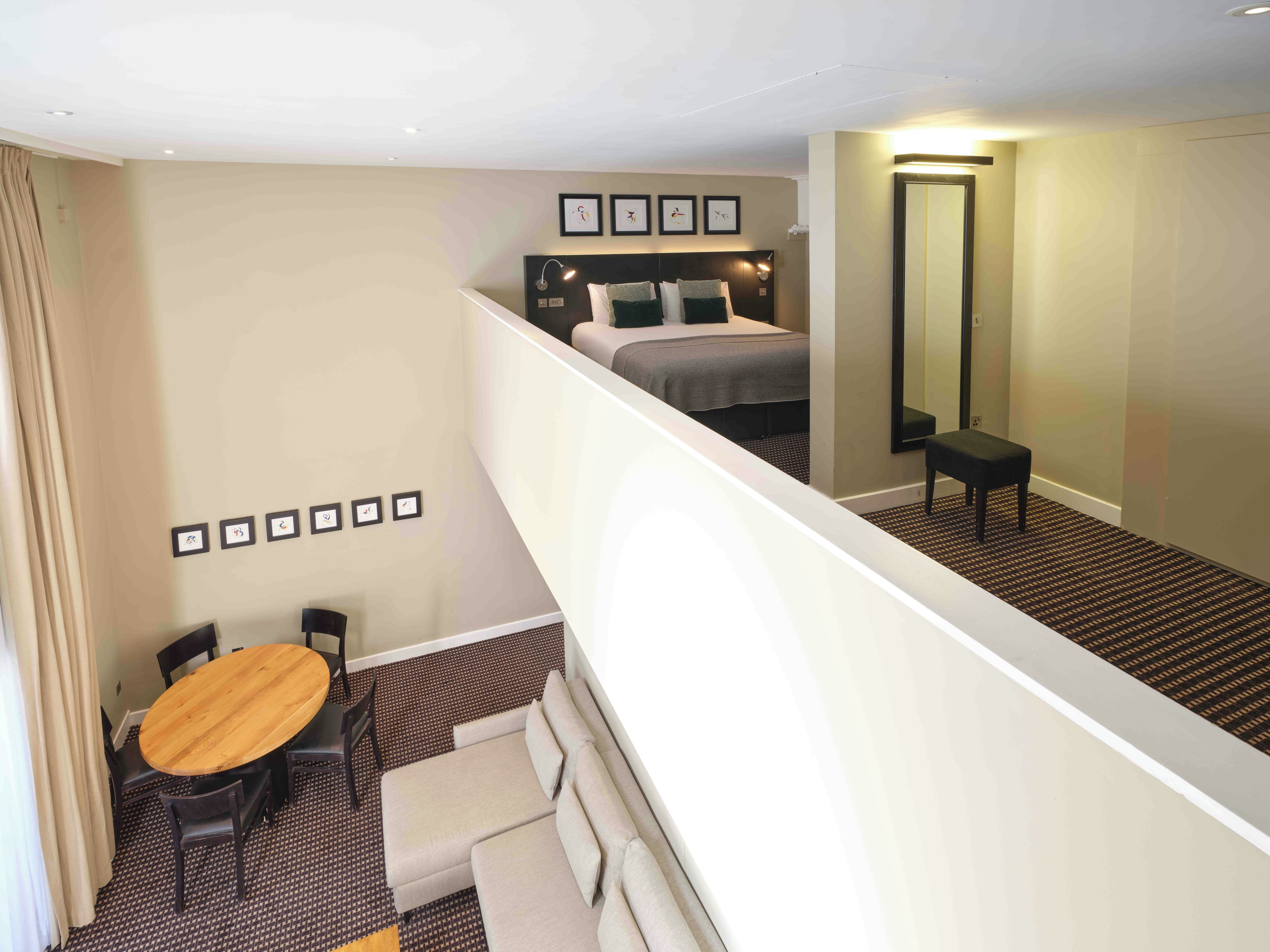 A hotel room with a bed, a desk, and a chair. There is a staircase leading to an upper level.