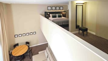 A hotel room with a bed, a desk, and a chair. There is a staircase leading to an upper level.