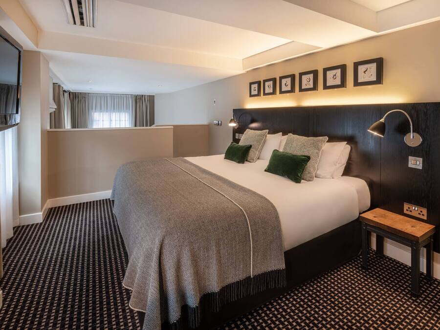 Camera d'albergo con un letto grande, un comodino, una TV e un'opera d'arte appesa al muro.