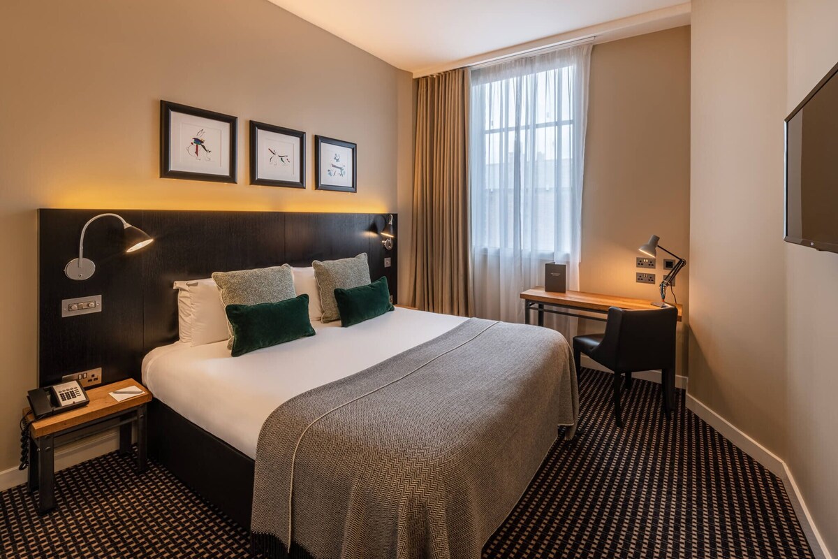 Une chambre d’hôtel avec un grand lit, un bureau, une chaise et une fenêtre avec des rideaux.