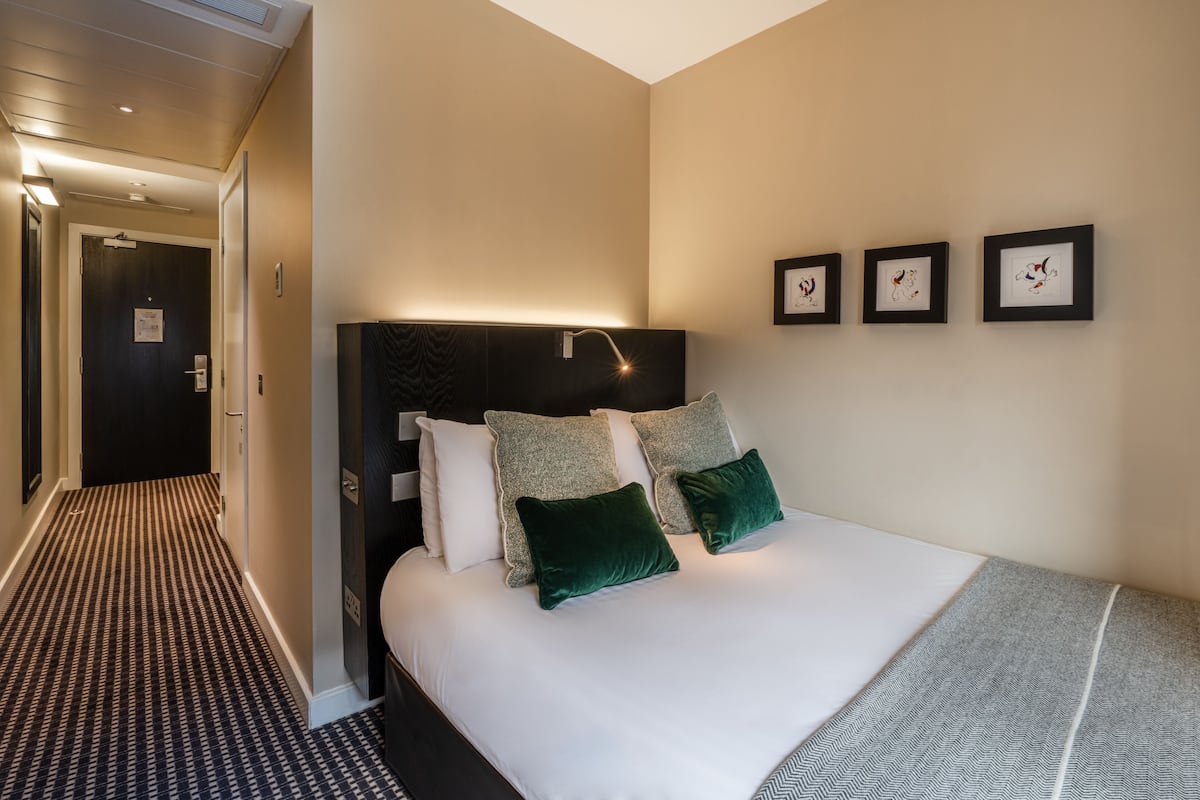 Ett hotellrum med en stor säng, en sänggavel och tre inramade tavlor på väggen.