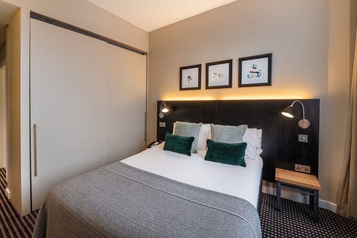 Ett hotellrum med en säng, sänglampor, ett nattduksbord och en väggklocka.